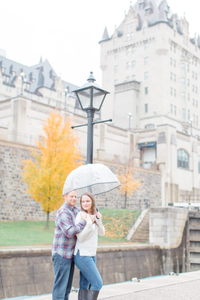Couple standing in the rain during engagement session Chateau Laurier in the background