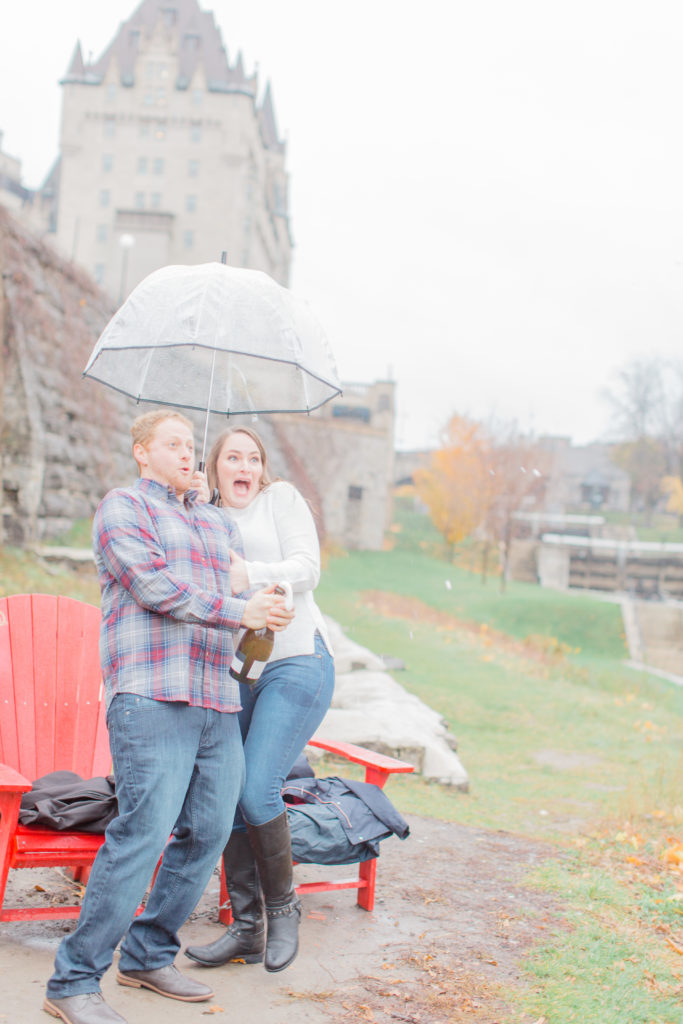 Couple standing in the rain during engagement session with the Chateau Laurier in the background popping bottle of champagne