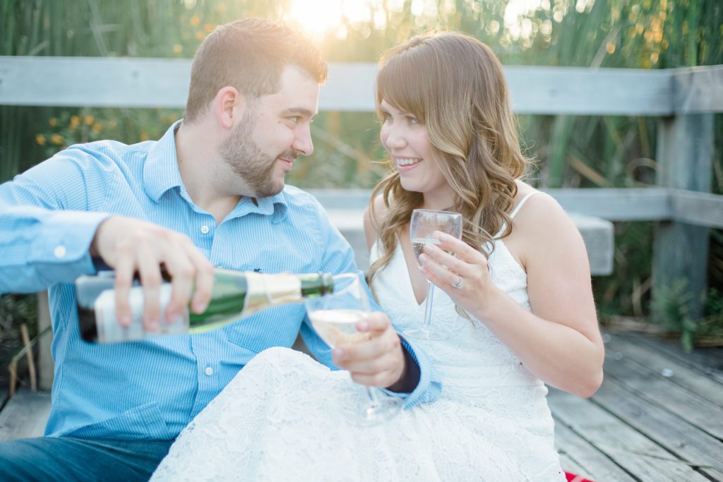 couple toasting champagne during an engagement session at mer bleue bog in ottawa east end wearing cute blue outfit with white dress