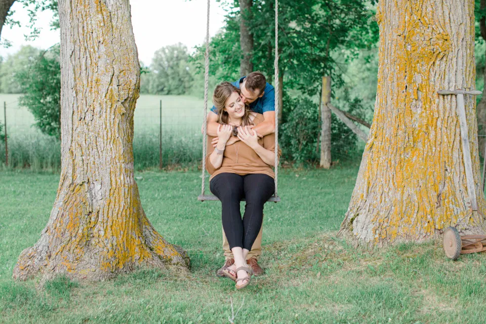 Swing between Trees - Engagement Session - Cow - Engagement Session Must Have Shot - Cows during Engagement Session - Poses during Engagement Session  Sunset - Natural Posing for Photo Session - Couples Photo Session Fun - Fun on the Farm - Farm Engagement Session - Blue and Brown Engagement Session Inspiration - Natural Engagement Session Posing - Ideas for what to wear for Engagement Photography, Modern Engagement Session Inspiration Wardrobe Ideas. Unsure of what to wear for your engagement photos, we've got you! Romantic brown with black leggings for Summer Engagement in Almonte. Grey Loft Studio is Ottawa's Wedding and Engagement Photographer for Real couples, showcasing photos that are modern, bright, and fun.